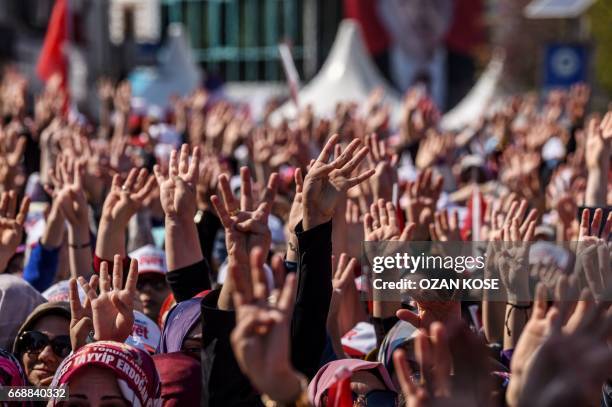 People cheer and flash a four finger sign called "the rabia sign" as the Turkish president delivers a speech in Istanbul, on April 15 during a rally...