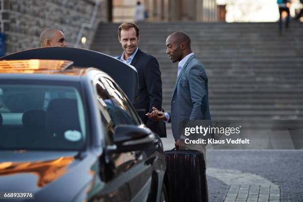 driver assisting businesspeople with luggage at taxi station - travel service stock pictures, royalty-free photos & images