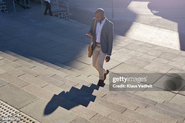 businessman looking at phone, while walking on staircase - businessman high angle stock-fotos und bilder