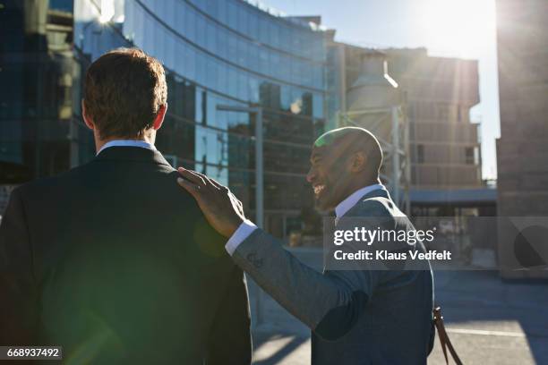 businessman tapping co-worker on the shoulder and laughing - man touching shoulder imagens e fotografias de stock