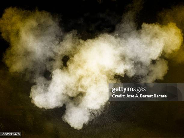 explosion of a cloud of powder of particles of  colors yellow and white on a black background - caer stockfoto's en -beelden