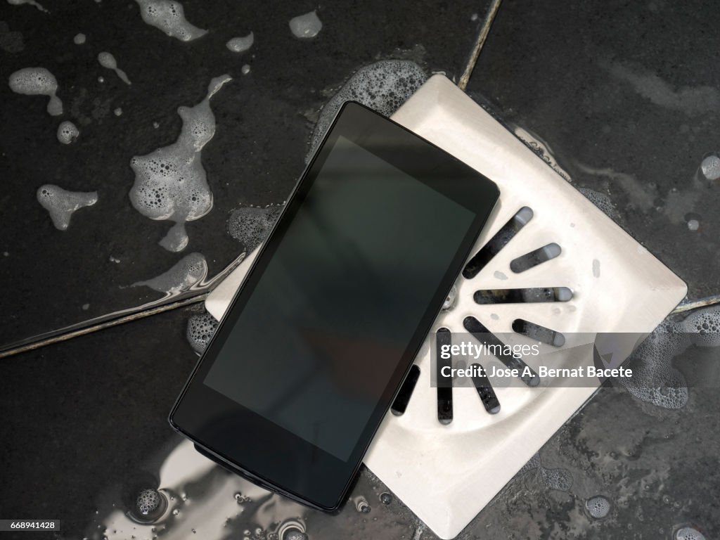 Smart mobile phone dropped on the floor of a shower next to the drain with water