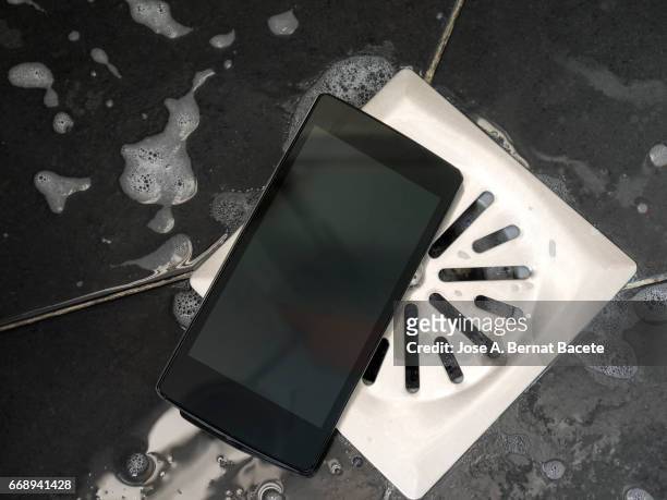 smart mobile phone dropped on the floor of a shower next to the drain with water - arruinado 個照片及圖片檔
