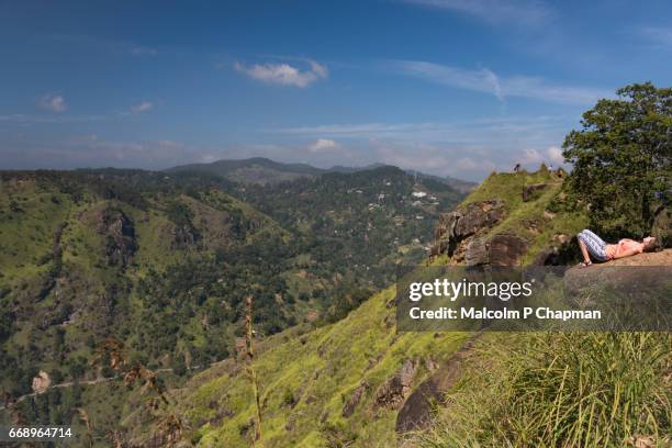 a tourist rests on a rock on little adam's peak with a steep drop below, ella, sri lanka - sri lanka little mountain fotografías e imágenes de stock