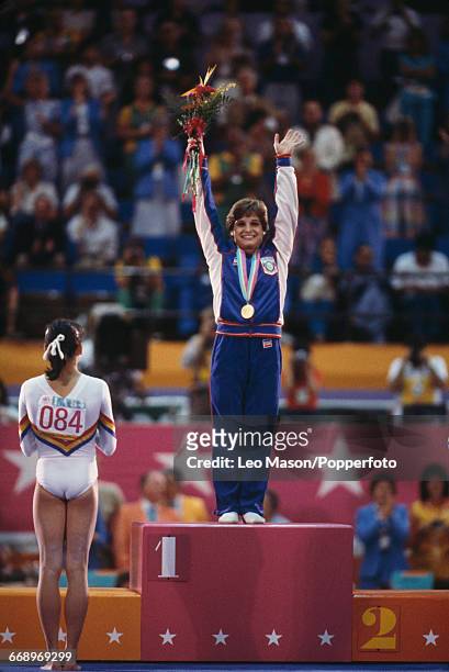American gymnast Mary Lou Retton stands on the podium and waves to the crowd after finishing in first place to win the gold medal in the Women's...