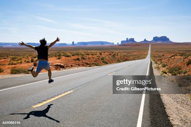 a man runs and jumps along a section of highway 163 in monument valley, utah, usa. - leap forward stock pictures, royalty-free photos & images