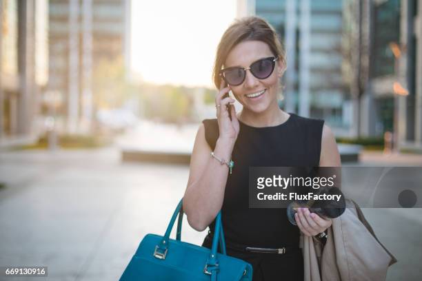 successful business woman smiling on the phone and holding coffee - blue purse stock pictures, royalty-free photos & images