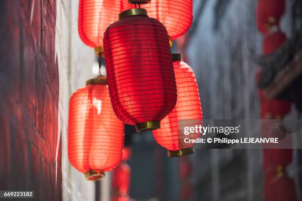 multiple red chinese lanterns in sunlight in a narrow street - chinese lantern stock pictures, royalty-free photos & images