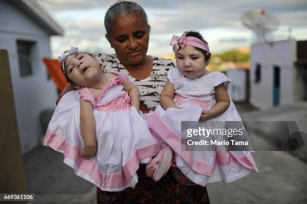 Grandmother Maria Jose holds her twin granddaughters Heloisa and Heloa Barbosa, both born with microcephaly, in front of their house as they pose for...