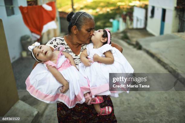 Grandmother Maria Jose holds her twin granddaughters Heloisa and Heloa Barbosa, both born with microcephaly, outside of their house as they pose for...