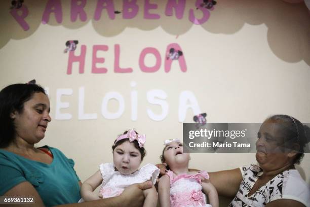 Mother Raquel Barbosa and grandmother Maria Jose hold twins Heloisa and Heloa Barbosa, both born with microcephaly, at their one-year birthday party...