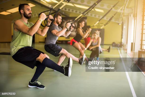 group of athletes doing strength exercises on suspension training in a health club. - suspension training stock pictures, royalty-free photos & images