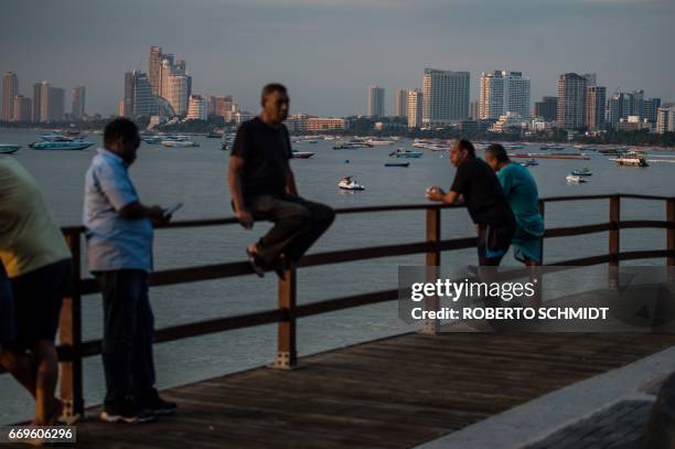 This photo taken on March 29, 2017 shows men leaning on a railing of a boardwalk off Beach Road during the late afternoon in Pattaya. Two hours east...