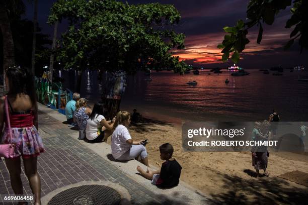 This photo taken on March 29, 2017 shows a woman walking past tourists and residents watching the sunset in Pattaya. Two hours east of Bangkok,...