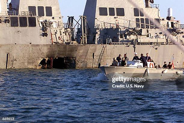 Navy and Marine Corps security personnel patrol past the damaged U.S. Navy destroyer USS Cole following the October 12, 2000 terrorist bombing attack...