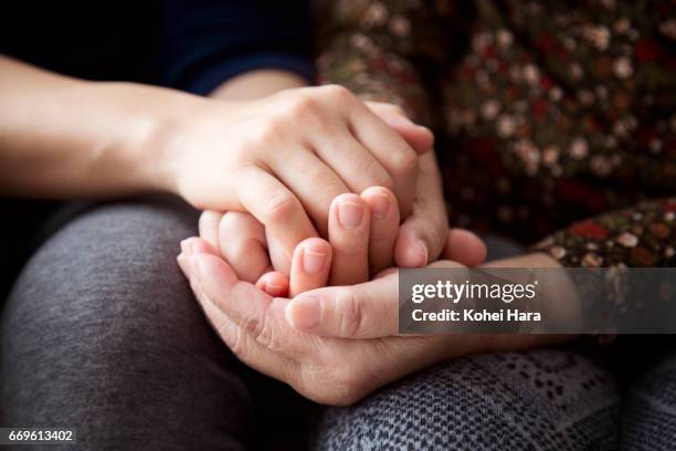 hands of a senior woman and her daughter holding each other's hands together - händchen halten stock-fotos und bilder