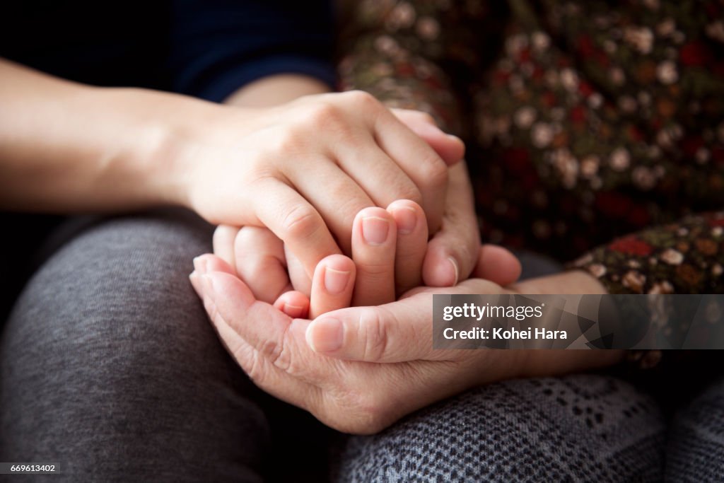 Hands of a senior woman and her daughter holding each other's hands together