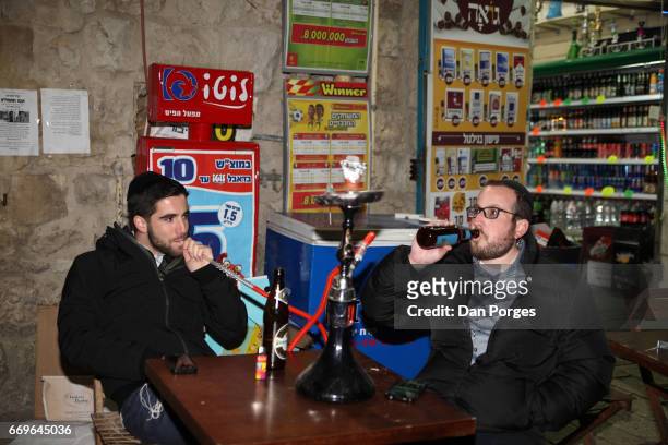 At a pub in the Nahalat Shiv'a neighborhood, a pair of young men, both with yarmulkes on their heads, sit at a table with bottles of beer before them...