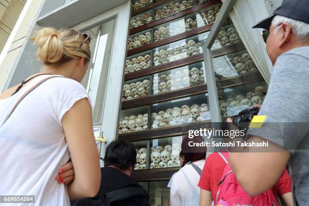 Foreign tourists look at human skulls displayed in a memorial tower at the Choeung Ek killing fields during a memorial service to mark the 42nd...