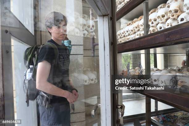 Man looks at human skulls displayed in a memorial tower at the Choeung Ek killing fields during a memorial service to mark the 42nd anniversary of...