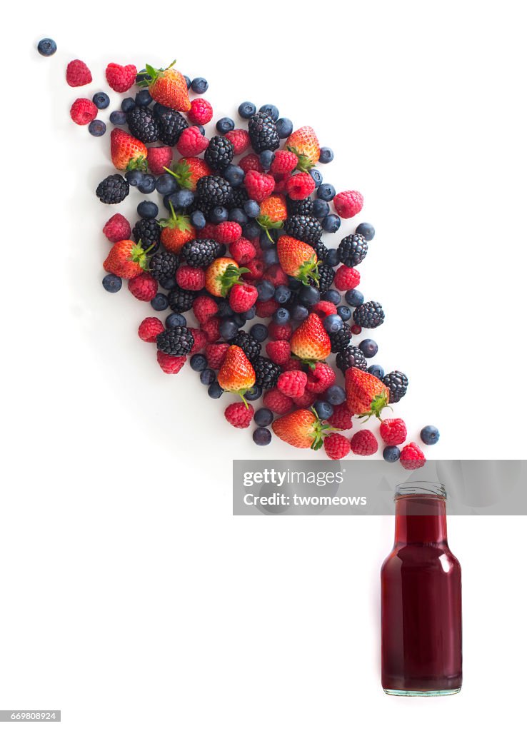 Flat lay assorted berry fruits flowing out from juice bottle.