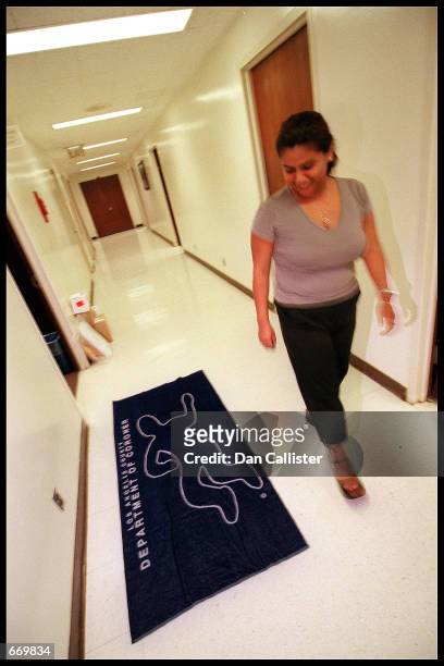 Woman walks past a beach towel with the chalk outline of a victim July 21, 2000 outside the Los Angeles County Coroners Gift Shop in Los Angeles.