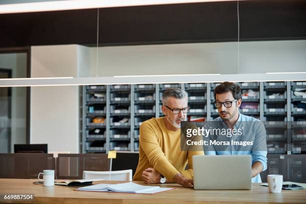 businessmen using laptop together at desk - mid adult men stock pictures, royalty-free photos & images