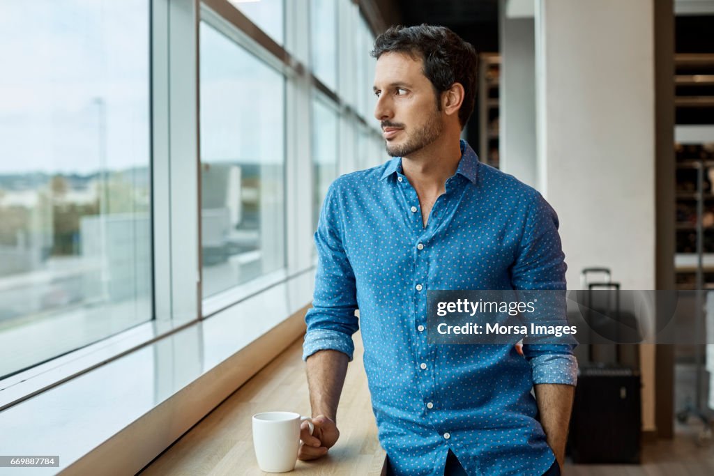 Thoughtful businessman with cup at window sill