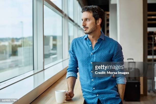 thoughtful businessman with cup at window sill - shirt stock pictures, royalty-free photos & images