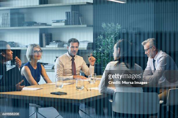 coworkers communicating at desk seen through glass - riunione foto e immagini stock