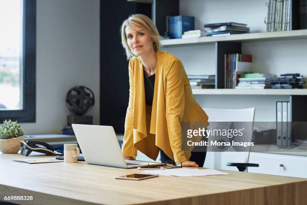 confident businesswoman leaning on desk - 35 39 anni foto e immagini stock