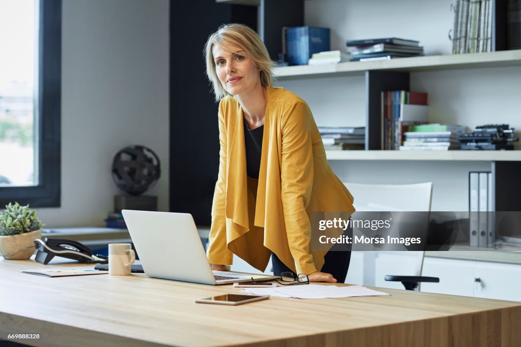 Confident businesswoman leaning on desk
