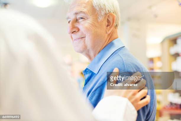 smiling senior man looking at pharmacist - pharmacy imagens e fotografias de stock