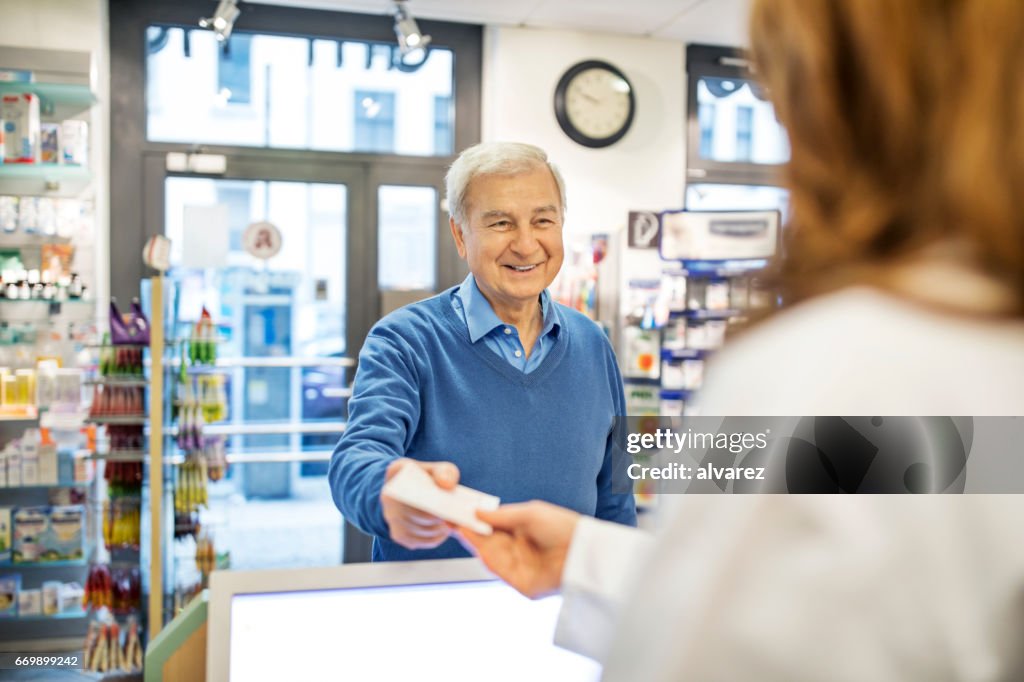 Smiling senior man giving prescription to chemist