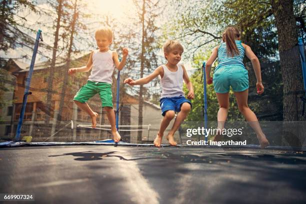 three kids jumping on large trampoline - trampoline stock pictures, royalty-free photos & images