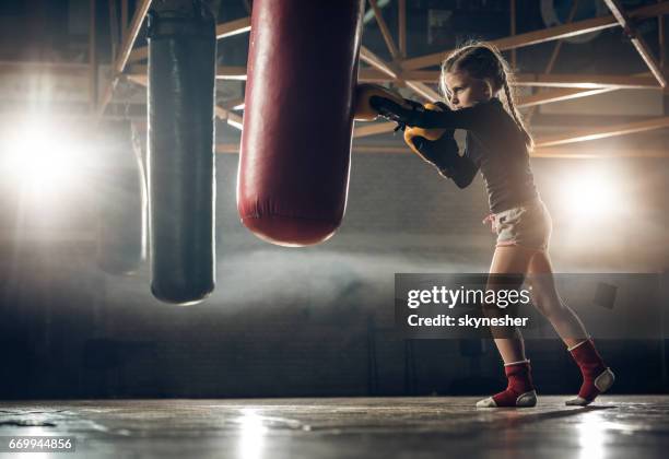 full length of determined little girl punching a bag on kickboxing training. - kids boxing stock pictures, royalty-free photos & images