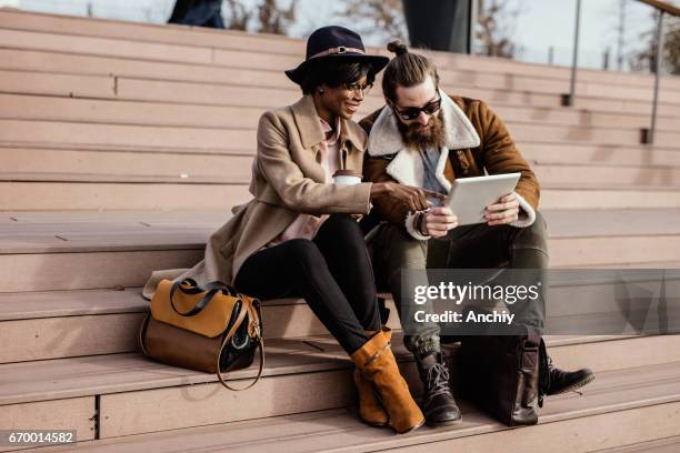 moda amigos sientan en el reloj de la escalera videos graciosos en un gadget portátil - woman boots fotografías e imágenes de stock