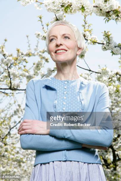 senior woman stands between blossoming cherry trees - gutaussehend fotografías e imágenes de stock