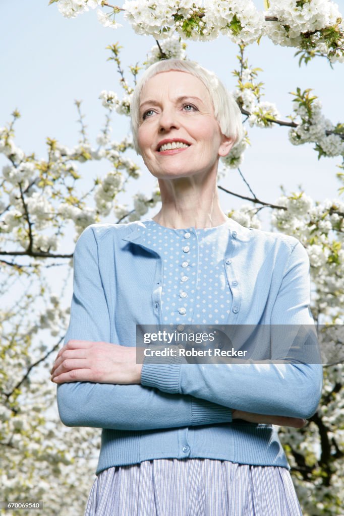 Senior woman stands between blossoming cherry trees
