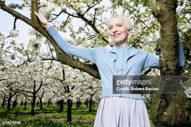 senior woman stands between blossoming cherry trees - weißes haar stock pictures, royalty-free photos & images