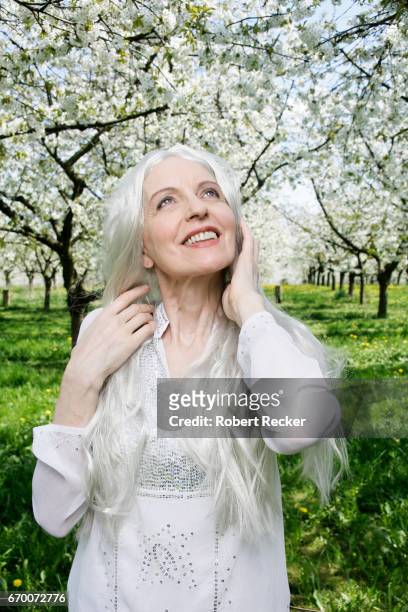 senior woman stands between blossoming cherry trees - sorglos foto e immagini stock