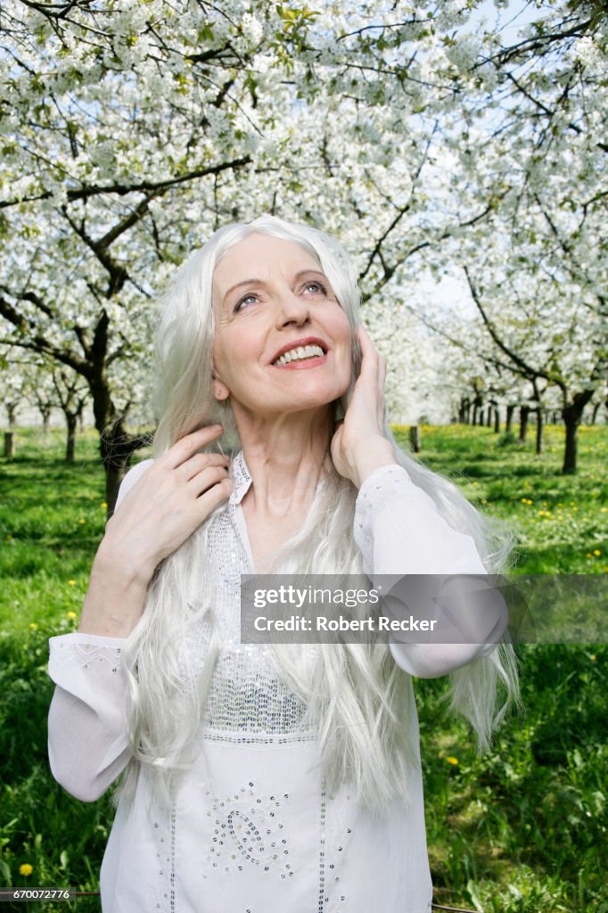 Senior woman stands between blossoming cherry trees