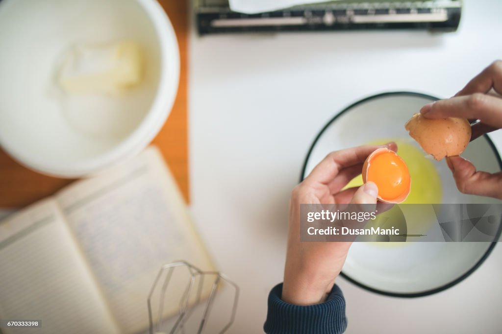 Female hands holding cracked egg over a white bowl