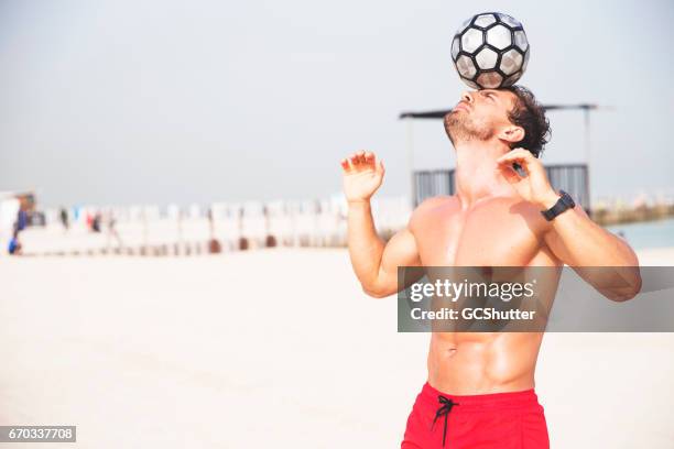 uomo che gioca con un calcio in spiaggia - portare sulla testa foto e immagini stock