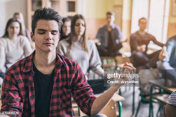 male student and his classmates practicing yoga in the classroom. - teenager meditating stock pictures, royalty-free photos & images