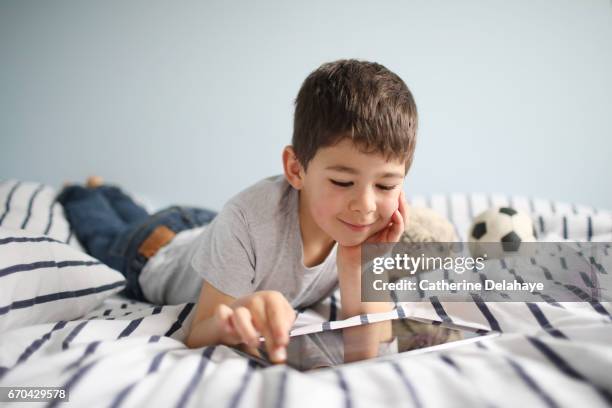 a boy with a tablet on his bed - tablette numérique stockfoto's en -beelden