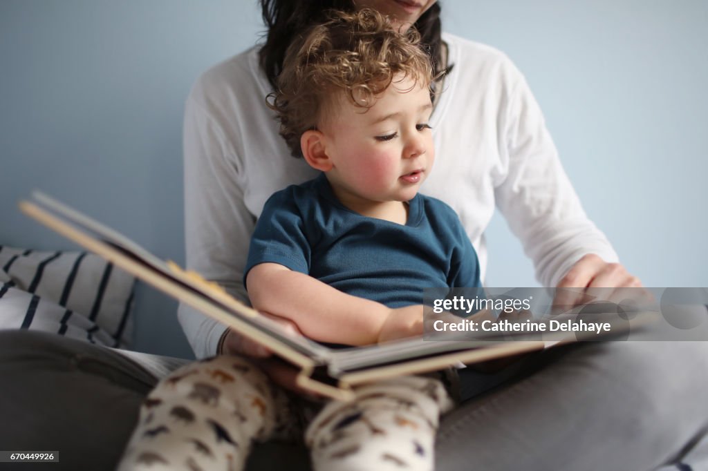 A 2 years old boy reading a book with his mom