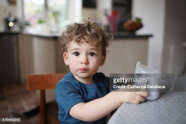a 2 years old boy drinking with a goblet in the the kitchen - 2 3 anni foto e immagini stock