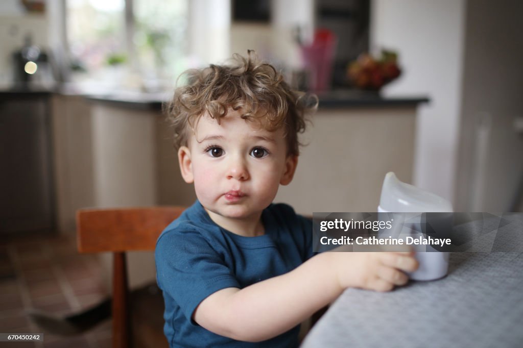 A 2 years old boy drinking with a goblet in the the kitchen
