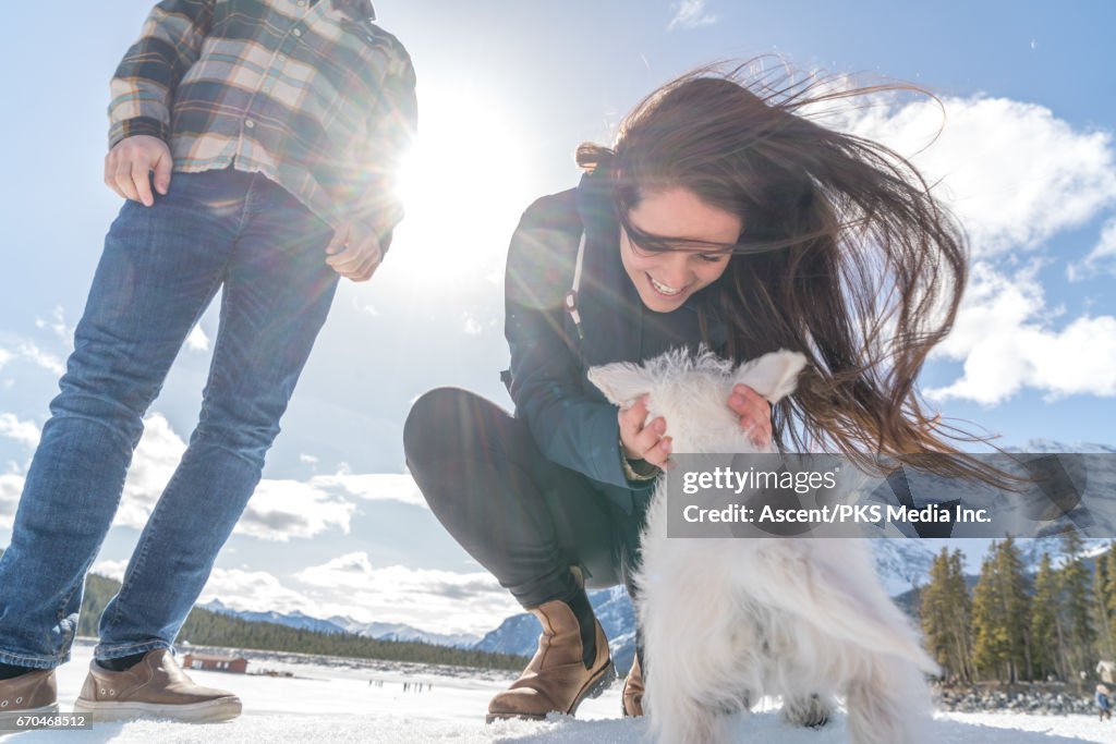 Young couple play with dog, in snowy mountain setting